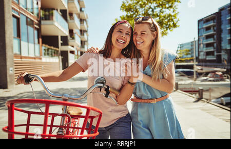 Due giovani amici di sesso femminile a piedi attraverso la città con le loro bici e divertirsi insieme Foto Stock