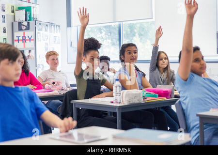 Studenti di scuola materna con le mani sollevate in aula Foto Stock