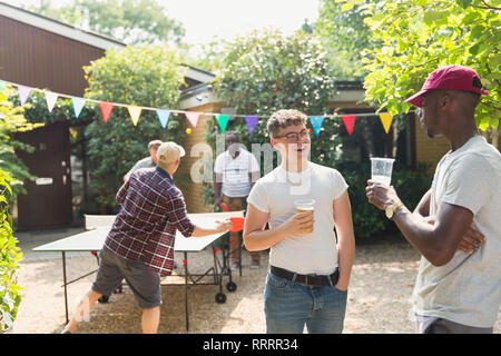 Amici maschi a bere birra e giocare a ping pong in estate nel cortile Foto Stock