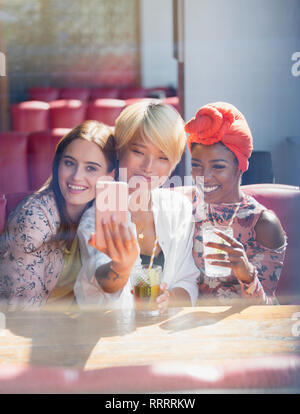 Giovani donne amici bevendo cocktail e posa per selfie nel soleggiato ristorante Foto Stock