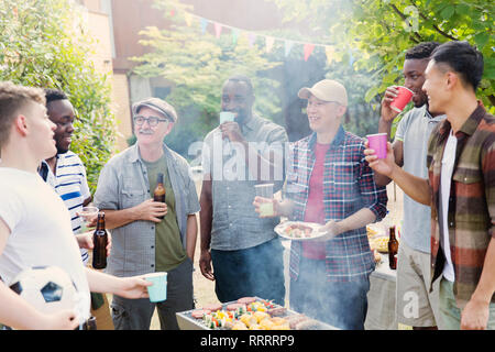 Amici maschi a bere birra attorno a un barbecue nel cortile posteriore Foto Stock