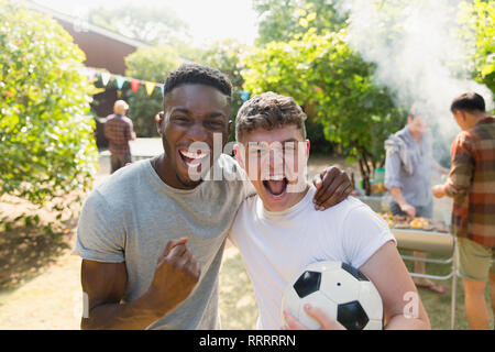 Ritratto di giovane entusiasta degli uomini con pallone da calcio tifo, godendo di back yard barbecue Foto Stock