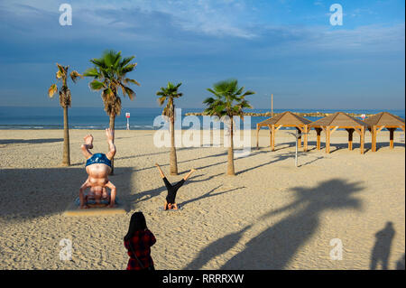 Giovane donna di scattare una foto del suo amico fare yoga accanto al Ben Gurion statua sulla spiaggia di Tel Aviv, Israele Foto Stock