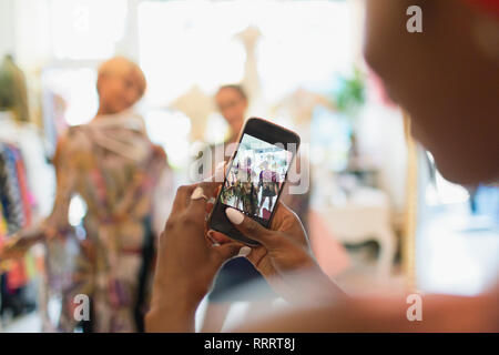 Giovane donna con la fotocamera del telefono a fotografare gli amici di shopping in negozio Foto Stock