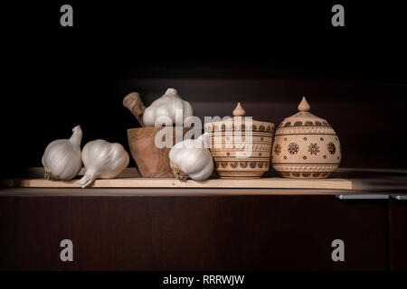 Natura morta con vasi di legno per le spezie, verniciato con folk ucraini, ornamento e mortaio di legno con il pestello per la macinazione di spezie e teste d'aglio, dri Foto Stock