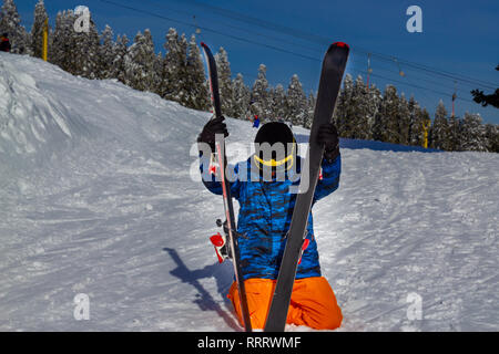 Giovane uomo seduto sulla neve e coppia ski Foto Stock