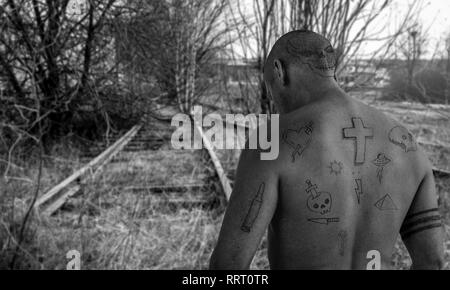 Ragazzo con doodle tatuaggi camminando sulla ferrovia abbandonata la via. Penale, condannare la fuga e il carcere tattoo concetto. Montaggio dell'immagine. Foto Stock