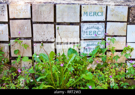 Molti di marmo bianco per le schede con una parola francese merci su un muro di pietra tra piante verdi e piccoli fiori di colore rosa Foto Stock