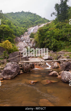 Un piccolo ponte di bambù attraversa un piccolo fiume di fronte a una cascata, Sa Pa, Vietnam Foto Stock