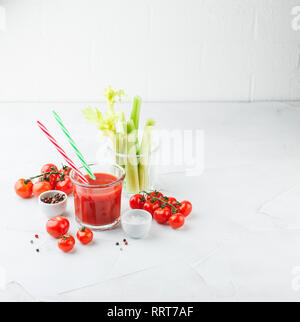 Bicchiere di deliziosi succhi di pomodoro con due cannucce rigate, gambi di sedano fresco, sale e pepe fresco e succosi pomodorini ciliegia su uno sfondo luminoso. B Foto Stock