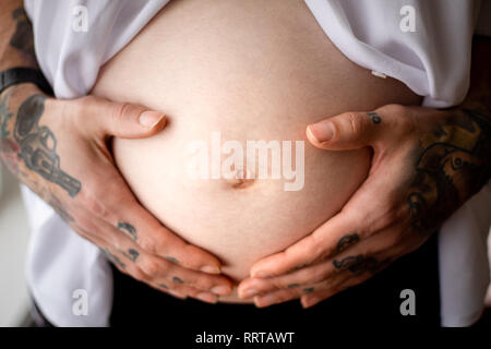 Le mani tatuate di papà la culla del ventre incinta Foto Stock