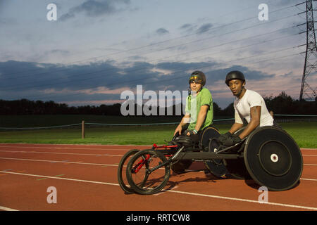 Ritratto fiduciosi atleti paraplegici formazione per sedia a rotelle gara su sport via di notte Foto Stock