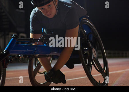 Ritratto determinata femmina e giovane atleta paraplegico formazione per sedia a rotelle gara su sport via di notte Foto Stock