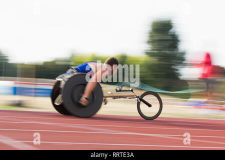Determinato maschile giovane atleta paraplegico accelerando lungo la via dello sport in carrozzella gara Foto Stock
