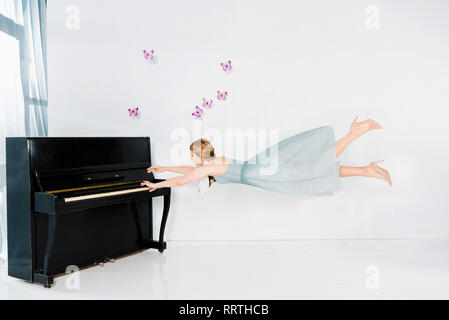 Ragazza flottante in vestito blu giocare nero pianoforte Foto Stock