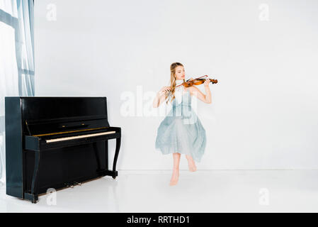 Ragazza flottante in vestito blu suona il violino su sfondo bianco Foto Stock