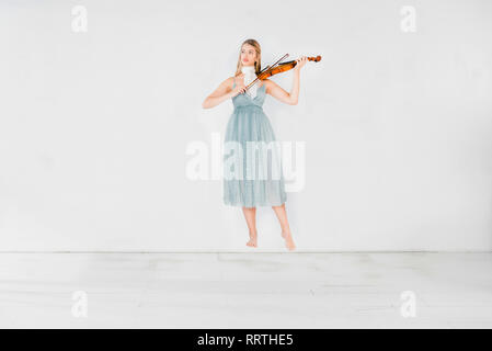 Ragazza flottante in vestito blu suona il violino su sfondo bianco con spazio di copia Foto Stock