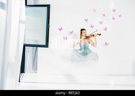 Ragazza flottante in vestito blu suona il violino su sfondo bianco Foto Stock