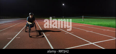 Ritratto fiduciosi, determinata femmina e giovane atleta paraplegico formazione per sedia a rotelle gara su sport via di notte Foto Stock