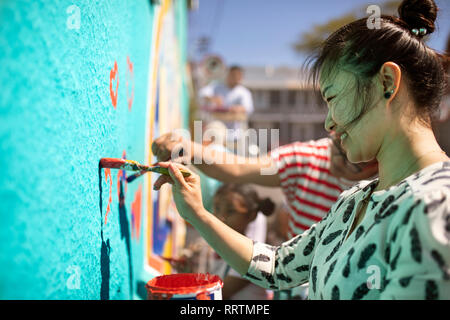 Donna sorridente volontario pittura murale sulla parete soleggiato Foto Stock