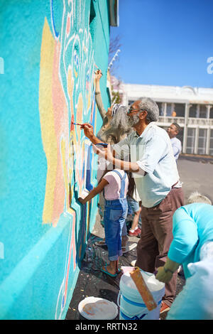 Volontari della comunità vibranti di pittura murale sulla soleggiata parete urbana Foto Stock