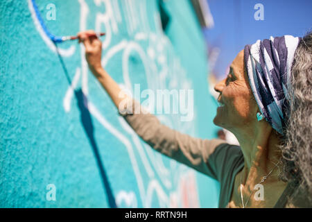 Senior donna pittura murale sulla parete soleggiato Foto Stock