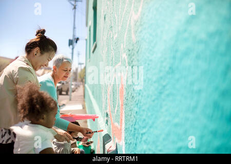 Volontari di sesso femminile pittura murale sulla parete soleggiato Foto Stock