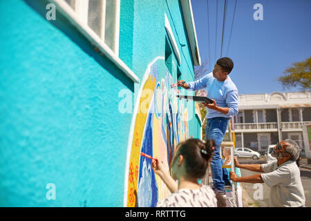 Volontari della comunità vibranti di pittura murale sulla soleggiata parete urbana Foto Stock