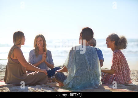 Happy amici parlano in cerchio sulla spiaggia soleggiata durante il ritiro di yoga Foto Stock