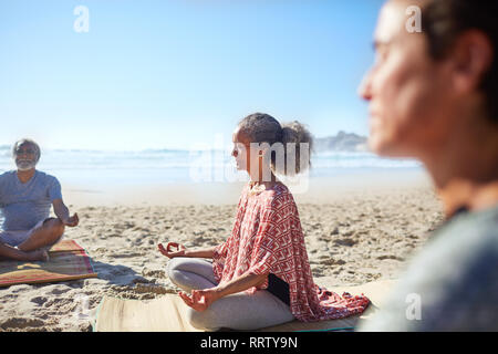 Serena donna senior meditando sulla spiaggia soleggiata durante il ritiro di yoga Foto Stock