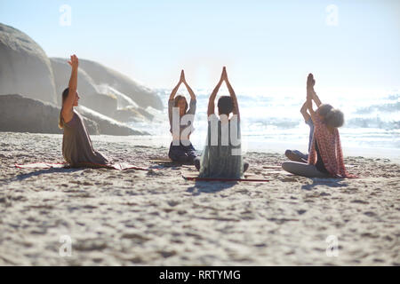 Serena la gente in cerchio meditando sulla spiaggia soleggiata durante il ritiro di yoga Foto Stock