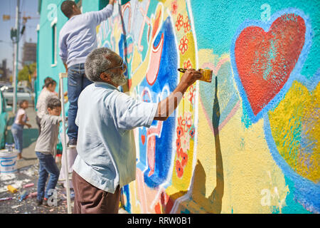 Senior uomo pittura murale sulla soleggiata parete urbana Foto Stock