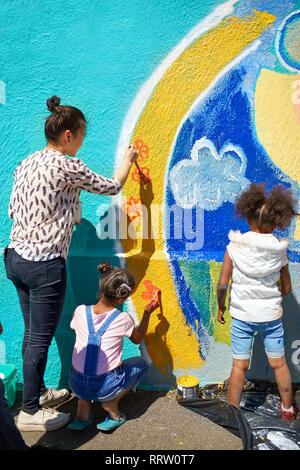 Madre e figlia volontari vibrante di pittura murale sulla parete soleggiato Foto Stock