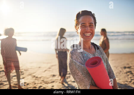 Ritratto di donna felice con materassino yoga sulla spiaggia soleggiata durante il ritiro di yoga Foto Stock