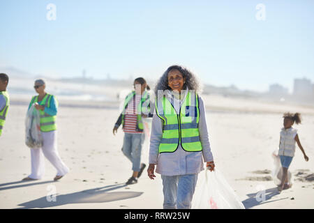 Ritratto fiducioso donna senior volunteer pulizia lettiera di sunny beach Foto Stock