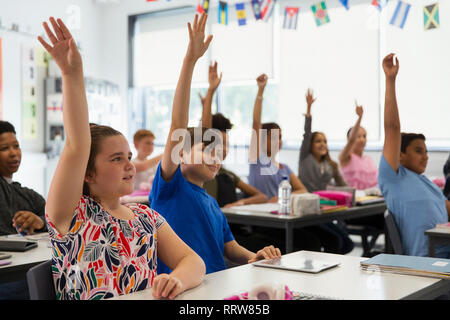 Desiderosi junior high school gli studenti con le mani sollevate in aula Foto Stock