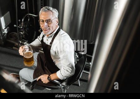 Vista aerea di sorridere senior brewer nel grembiule tenendo un bicchiere di birra nella birreria Foto Stock