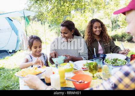 La famiglia felice godendo il pranzo al tavolo di campeggio Foto Stock