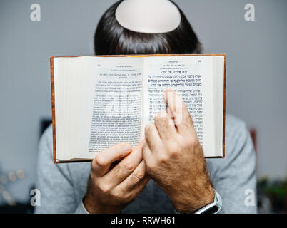 Maschio ebreo indossando kippa , lettura orante bi-lingue ebraico mahzor francese libro di preghiera da 1920 utilizzato in alto i Giorni santi di Rosh Hashanah e Yom Kippur puntano al testo. Foto Stock