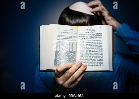 Maschio ebreo indossando kippa , lettura orante bi-lingue ebraico mahzor francese libro di preghiera da 1920 utilizzato in alto i Giorni santi di Rosh Hashanah e Yom Kippur - bollino blu. Foto Stock
