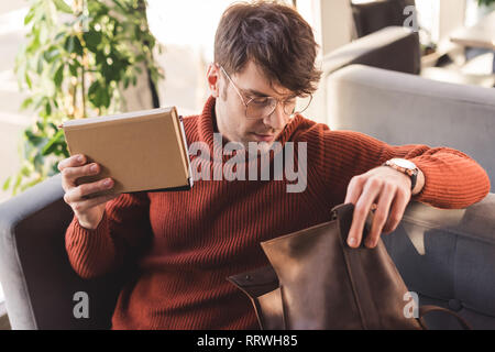 Uomo bello in bicchieri contenere libri e guardando il sacchetto in cafe Foto Stock