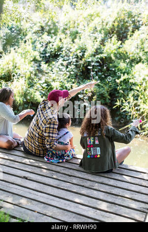 Famiglia soffiare bolle sul dock di boschi Foto Stock