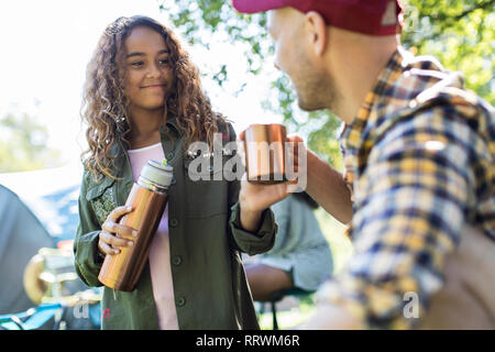 Figlia versando caffè isolato dal contenitore per bevande fro padre al campeggio Foto Stock