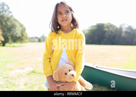 Ragazza con Teddy bear nel campo soleggiato con canoa Foto Stock