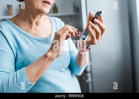 Vista ritagliata della donna senior utilizza lo smartphone a casa Foto Stock