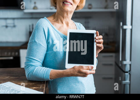 Vista ritagliata della donna senior presentando tavoletta digitale con schermo vuoto a casa Foto Stock