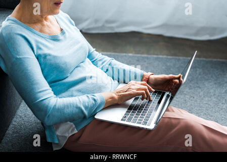 Vista ritagliata della donna senior di digitazione sul portatile a casa Foto Stock