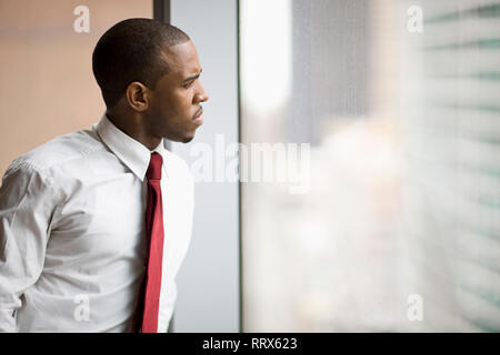 Mid-adulto uomo d affari di guardare attraverso una finestra. Foto Stock