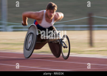 Determinato maschile giovane atleta paraplegico accelerando lungo la via dello sport in carrozzella gara Foto Stock