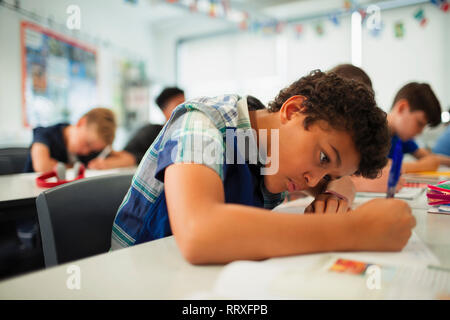 Focalizzato junior high school boy facendo i compiti in classe Foto Stock